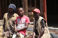 Three men standing together outdoors on coffee farm in Kenya, with one wearing a red cap and another in a pink shirt.